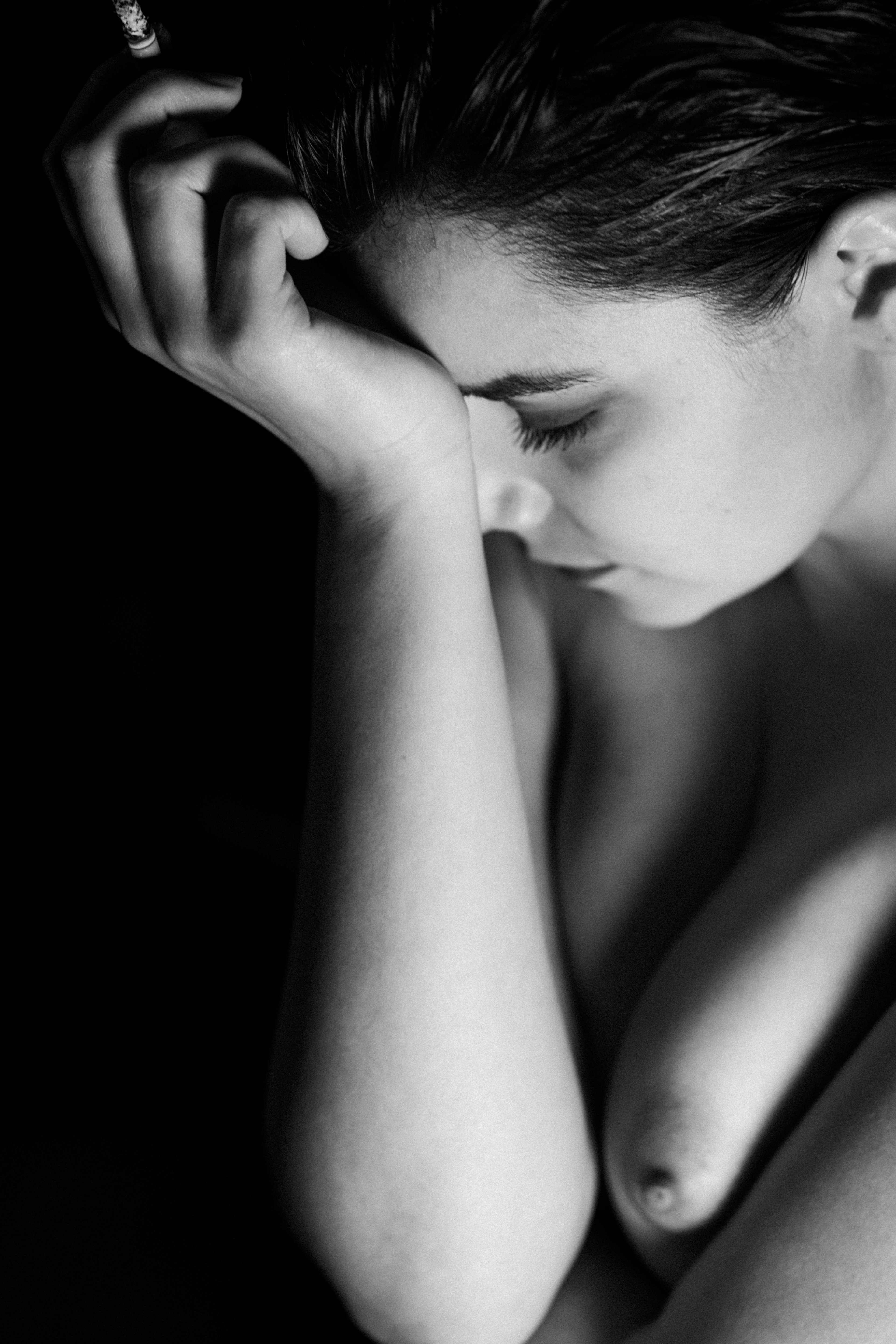 Primo piano in bianco e nero di una donna con fronte appoggiata all’avambraccio; occhi chiusi, spalla e seno parzialmente visibili, luce laterale morbida.